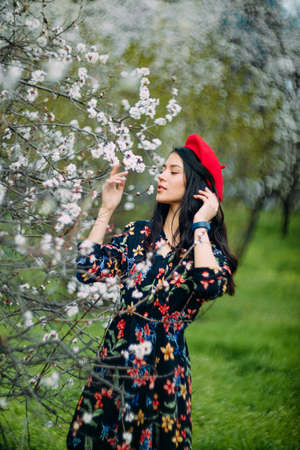 A young brunette woman stands and enjoys in garden among the spring blossoming apricot trees.の写真素材
