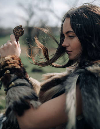 Woman sits and rests on grass in forest in image of ancient warrior amazon with sword in her hands. Portrait.の写真素材