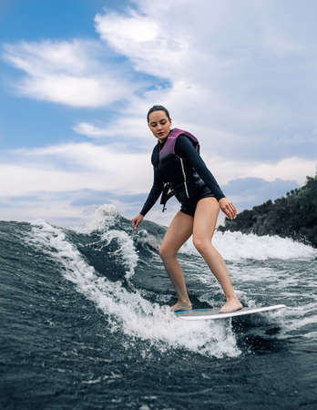 Young woman wakesurfing on wave from a motorboat against baskground of sky.の写真素材