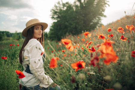 Young woman in straw hat enjoys by flowering poppies among meadow. Copy space.の写真素材