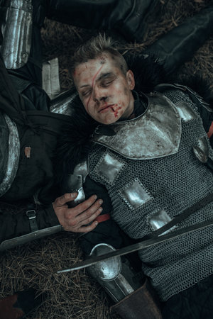 Tired medieval knight lies and sleeps on the ground near his sword.の写真素材