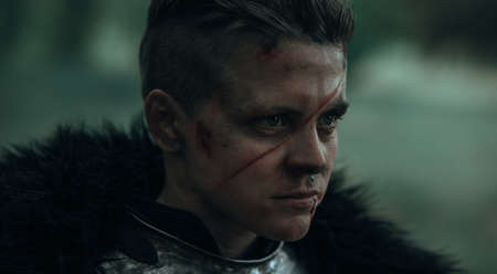 Portrait of medieval warrior knight in armor with bloody face and scar.