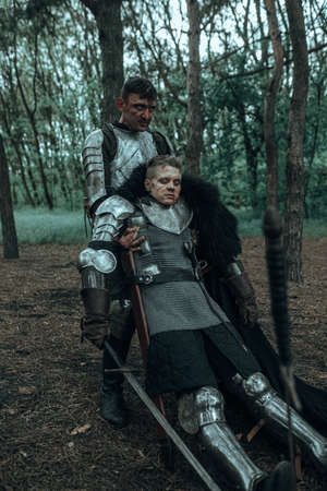 Medieval knight in chain mail armor drags on the ground warrior wounded in battle among forest.の写真素材