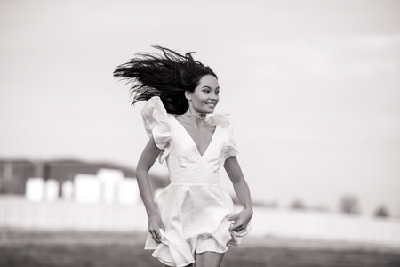 Young joyful woman in white dress runs in meadow on summer sunny day. Black and white image. Closeup.の写真素材