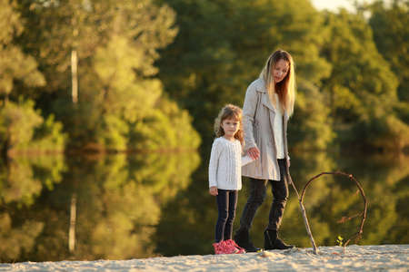 Mother walks together with her daughter on beach near river.の写真素材