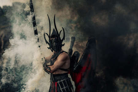 Man in image of daemon of death with wings behind his back stands with raised black sword in his...