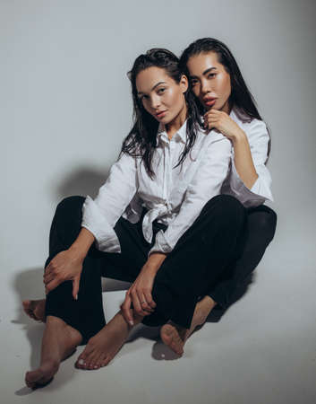 Two young women with wet hair and water drops on face pose sitting in studio.の写真素材