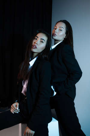 Two young brunette women pose in studio standing dressed in black suits.の写真素材