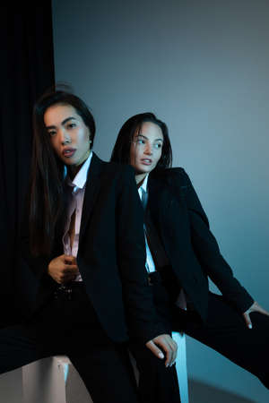 Two young brunette women pose in studio standing dressed in black suits.の写真素材