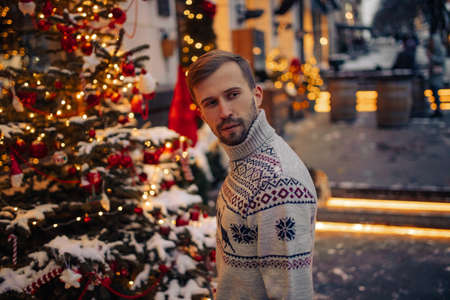 Portrait of young thoughtful man in street decorated for Christmas against background of glowing garlands.の写真素材
