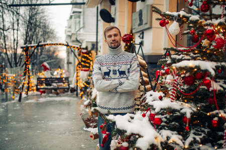 Young man stands and smiles near building in snowy street decorated for Christmas.の写真素材