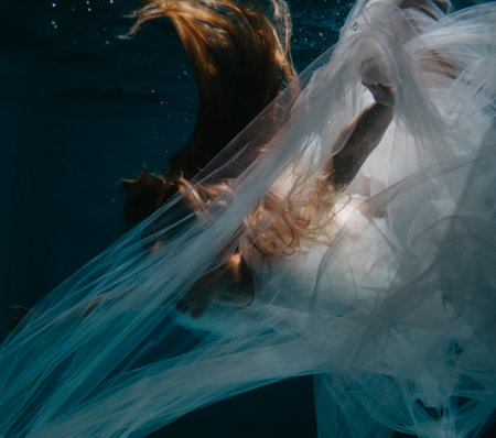 Beautiful young woman in bridal dress swims and dives under sunlit deep water. closeup.の写真素材