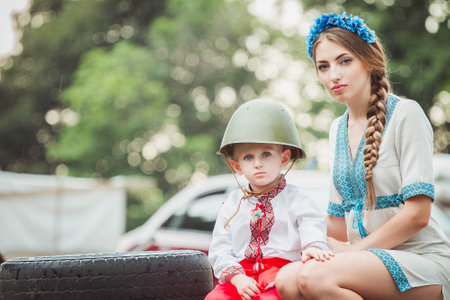 Young ukrainian woman sits with child boy in traditional national dress on roadblock near tire. Concept of Russian military invasion in Ukraine. War in Ukraine and Europe. children and war.の写真素材