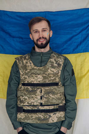 Portrait of young man in body armor against background of Ukrainian flag. Concept of Russian military invasion in Ukraine. War in Ukraine and Europe.の写真素材