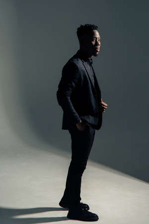 Young african man in jacket stands against gray background.