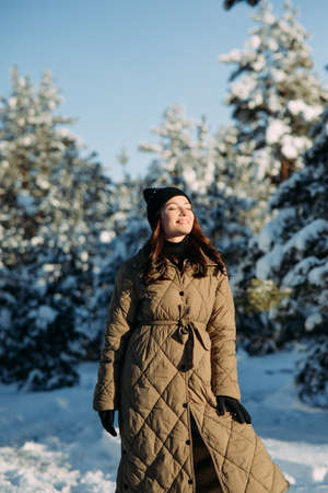 Happy young smiling woman walks in forest among snow-covered pine trees in sunny winter day.の写真素材