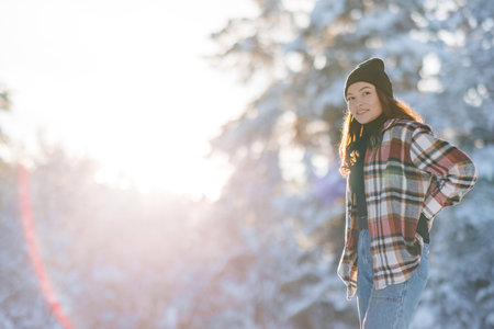 Happy young smiling woman walks in forest among snow-covered pine trees in sunny winter day.