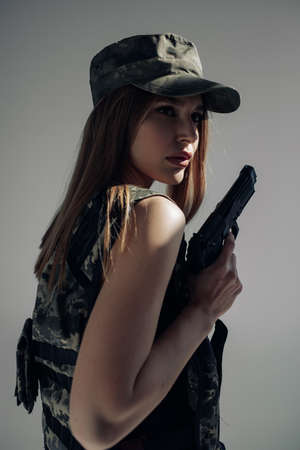 Portrait of young woman in uniform with handgun in her hand against gray background.の写真素材