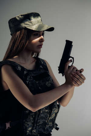Portrait of young woman in uniform with handgun in her hand against gray background.の写真素材