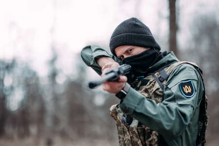 Young man practices and aims from pump gun weared in body armor and balaclava in the forest. closeup.の写真素材