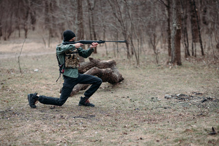 Young man practices and aims from pump gun weared in body armor and balaclava in the forest.の写真素材