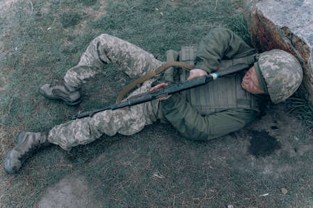 Ukrainian wounded soldier lying down on grass near rock after battle against russian enemy. Concept of Russian military invasion in Ukraine. War in Ukraine and Europe.の写真素材