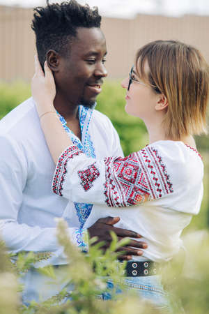 Interracial couple embraces in spring garden dressed in Ukrainian traditional ethnic embroidered shirts. Concept of love relationships and unity between different human races.の写真素材