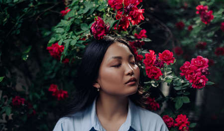 Portrait of young asian woman with closed eyes enjoying by blooming red climbing rose in garden.の写真素材