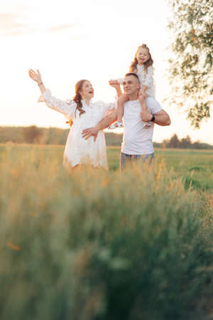 Happy family walks on meadow and father carries daughter on his shoulders during outing.の写真素材