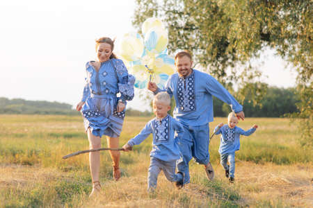 Happy parents with two of their twins sons have fun and run on meadow with air balloons. They are...