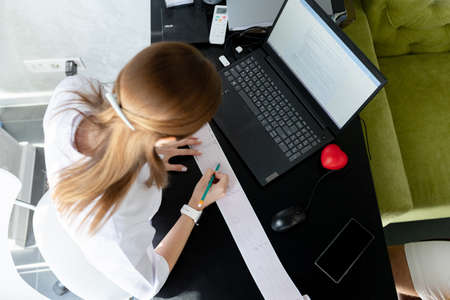 Woman cardiologist doctor sits at desk and decodes electrocardiogram graph printout in clinic. Test,...