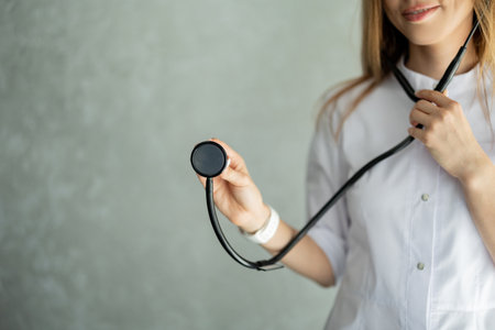 Woman doctor stands and holds stethoscope against gray background. Concept of disease diagnostic and treatment. healthcare, medical service. Image with copy space.の写真素材