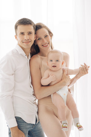 Young happy parents with their baby boy hold and embrace him against white background.の写真素材