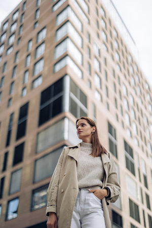 Young pretty woman in cloak walks on street against background of high building. closeup.
