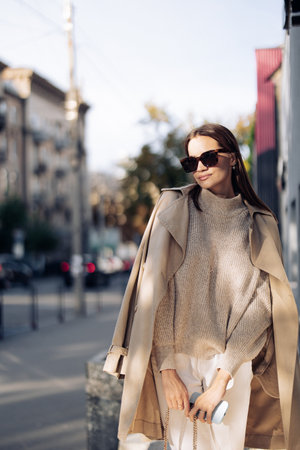 Young pretty woman in sunglasses and cloak walks on street against background of buildings. closeup.の写真素材