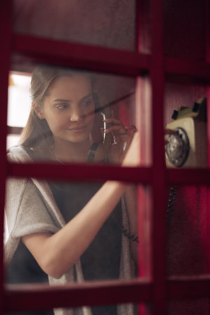 View through the glass to young woman dialing phone number in payphone booth. closeup.