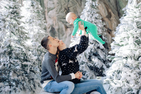Happy parents with baby son play in studio among Christmas trees decorated by artificial snow.の写真素材