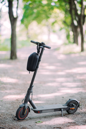 Electric scooter with bag is on the pathway in park against trees background.の写真素材