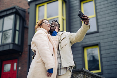 Young interracial couple takes a selfie together on street against background of houses. Concept of...