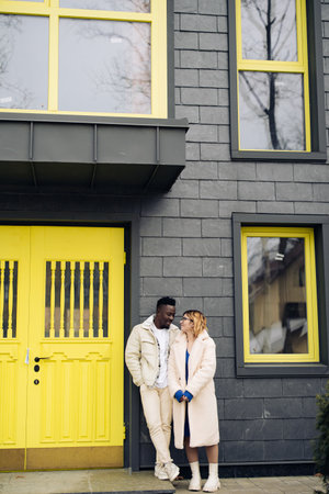 Young interracial couple stands and talks each other on street near house. Concept of love...