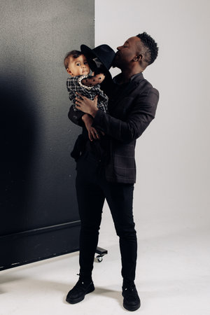 Young african man stands and holds on arms his baby daughter from interracial marriage. Concept of interracial family and unity between different human races.の写真素材