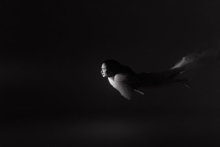 Underwater shoot of beautiful woman in white flying transparent dress swimming in illuminated water through light. Fantasy mermaid against water background with ray of light. Black and white image.の写真素材