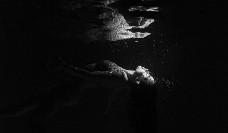 Underwater shoot of beautiful woman swimming and relaxing in water in sunbeams. Fantasy mermaid against water surface background with rays of lights. Black and white image.の写真素材