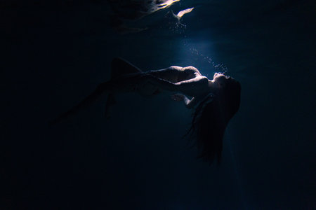 Underwater shoot of beautiful woman swimming and relaxing in water in sunbeams. Fantasy mermaid against water surface background with rays of lights.の写真素材