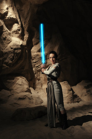 Kyiv, Ukraine - April 14, 2023: Cosplayer girl portrays character Rey Skywalker from the Star Wars universe with blue blade lightsaber in her hand among sandy canyon.のeditorial素材