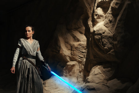 Kyiv, Ukraine - April 14, 2023: Cosplayer girl portrays character Rey Skywalker from the Star Wars universe with blue blade lightsaber in her hand among sandy canyon.のeditorial素材