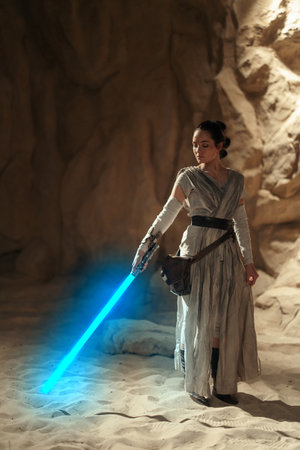 Kyiv, Ukraine - April 14, 2023: Cosplayer girl portrays character Rey Skywalker from the Star Wars universe with blue blade lightsaber in her hand among sandy canyon.のeditorial素材