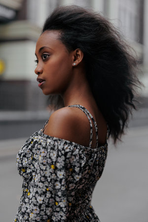 Portrait of young african sad woman in summer dress standing in city against background of building. side view.の写真素材