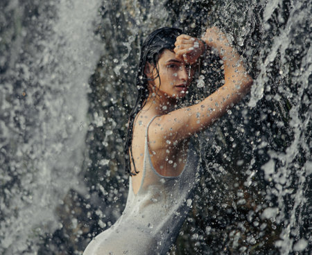 Portrait of young woman in wet dress standing in waterfall between water flows, spray and drops. closeup.の写真素材