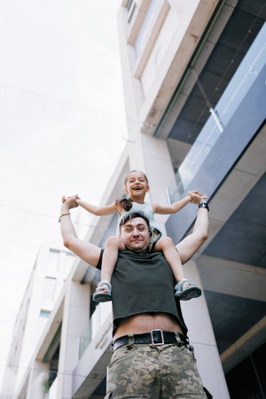 Little Ukrainian girl meets her father from the war during his vacation and cheerful plays with him. War in Ukraine. Russian military invasion in Ukraine. War and children.の写真素材